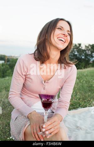 Reife Frau lachend beim Rotwein trinken im park Stockfoto