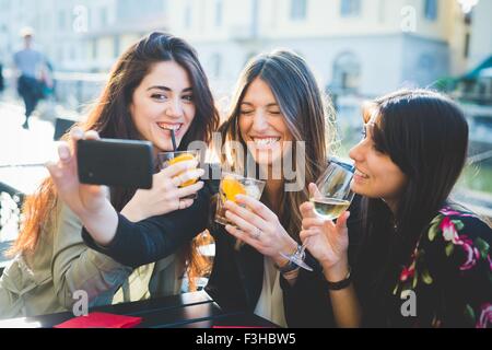 Drei junge Frauen kichern für Smartphone Selfie im Waterfront café Stockfoto