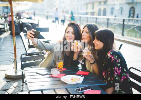 Drei junge Frauen posieren für Smartphone Selfie im Waterfront café Stockfoto