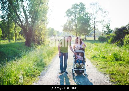 Mitte erwachsenes paar mit Kleinkind Tochter im Kinderwagen spazieren im park Stockfoto