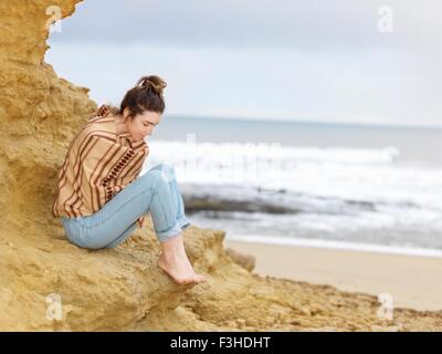 Junge Frau eingewickelt in Schal sitzt auf Klippen, Punkt Addis, Anglesea, Victoria, Australien Stockfoto