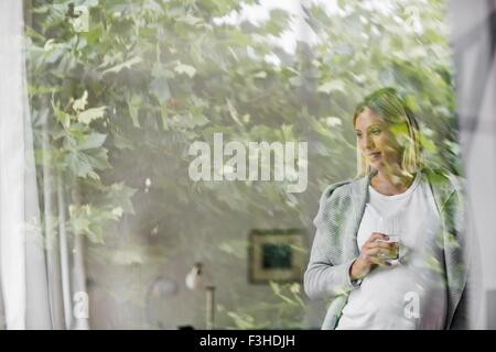 Volle Amtszeit Schwangerschaft junge Frau zu Hause hinter Fenster Stockfoto