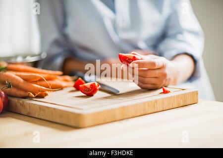 Beschnitten, Schuss volle Amtszeit Schwangerschaft junge Frau slicing Tomate in Küche Stockfoto