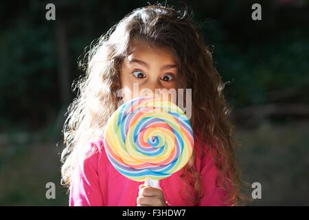 Porträt von Mädchen Kreuzung Augen mit Lollipop vor ihr Gesicht im Garten Stockfoto