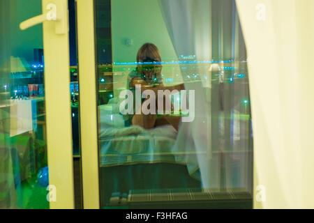 Junge Frau sitzt auf dem Bett im Zimmer Stockfoto