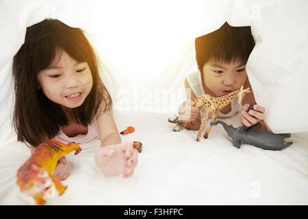 Chinesischen jungen und Mädchen im Bett spielen mit ihren Spielsachen unter der Bettwäsche Stockfoto