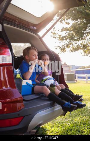 Junge und jüngere Schwester sitzen im Auto boot essende Orangen auf Fußball-Praxis-Pause Stockfoto