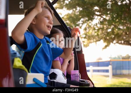 Junge und jüngere Schwester sitzen im Auto boot Fußball gucken Stockfoto