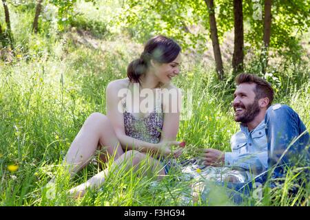 Junges Paar liegen auf dem Rasen von Angesicht zu Angesicht Essen Erdbeeren lächelnd Stockfoto