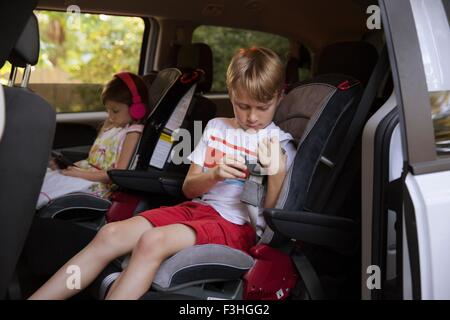 Mädchen mit digital-Tablette während Bruder befestigt Sicherheitsgurt im Auto Rücksitz Stockfoto