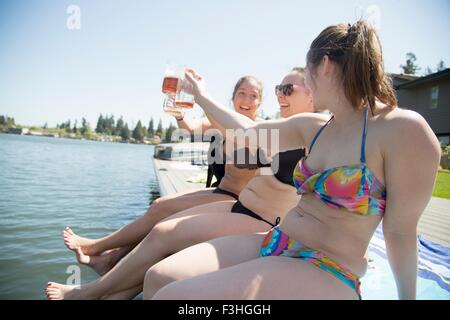 Junge Frauen tragen Bikinis Toasten mit Bier auf Waterfront Pier, Lake Oswego, Oregon, USA Stockfoto