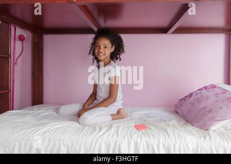 Mädchen tragen Pyjama kniend auf Bett, Blick auf die Kamera zu Lächeln Stockfoto