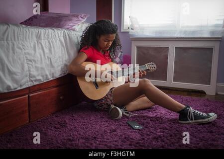 Mädchen sitzen auf dem Boden des Schlafzimmers spielt Gitarre, die auf der Suche nach unten Stockfoto