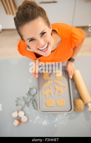 Lustige moderne Hausfrau hält Tablett mit rohem Halloween Kekse in Küche. Halloween behandelt bereit in Ofen gehen. Traditionelles Herbstferien. Obere Ansicht Stockfoto