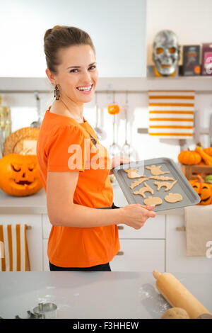 Fröhliche moderne Frau Tablett mit ungekochten Halloween Kekse bereit ins Ofen in der Küche zu halten. Traditionelles Herbstferien. Stockfoto