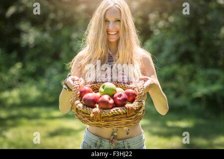 Porträt der jungen Frau hält Korb mit frischen Äpfeln im Garten Stockfoto