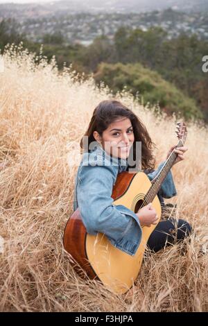 Porträt der jungen Frau spielt akustische Gitarre auf grasbewachsenen Hügel Stockfoto