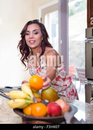 Mitte Erwachsene Frau Abholung Orange aus Obstschale Stockfoto