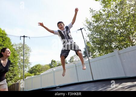 Mutter schaut Sohn springen auf dem Trampolin im Garten Stockfoto