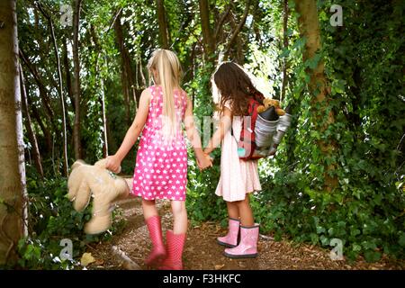 Ansicht von hinten von zwei Mädchen mit Teddybär und Rucksack wandern im Wald Stockfoto