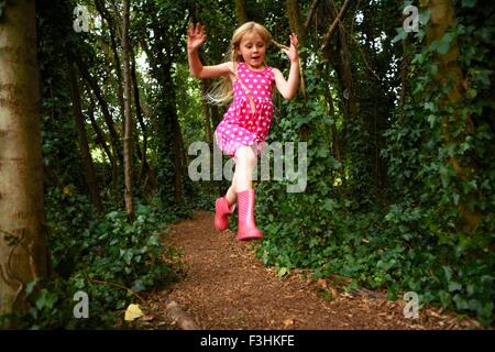 Mädchen tragen rosa Kleid und Kautschuk Stiefel springen im Wald Stockfoto