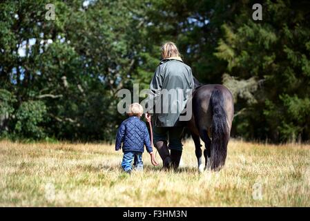 Rückansicht des Mutter und Sohn zu Fuß Pony im Feld Stockfoto