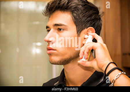 Kopf und Schultern enger bis der attraktive junger Mann mit dunklen Spritzen Ohr Haarspray in Ohren als Teil von morgen Pflege in die Flucht Stockfoto