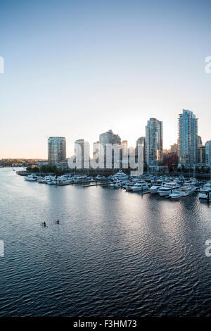 VANCOUVER, BRITISH COLUMBIA, KANADA. Zwei Ruderer paddeln Sie durch ruhiges Wasser mit Skyline Innenstadt in Ferne, von einer Brücke erschossen. Stockfoto