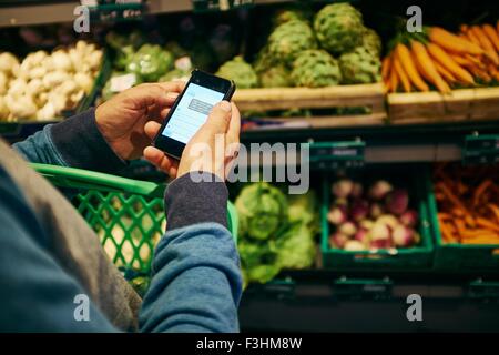 Mann einkaufen und mit Smartphone in Supermarkt Stockfoto