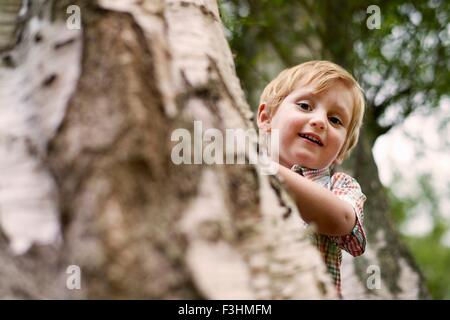 Junge spähen hinter Baum, Blick auf die Kamera zu Lächeln Stockfoto