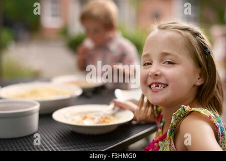 Mädchen am Gartentisch, Speisen über Schulter lächelnd in die Kamera schaut Stockfoto