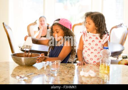 Schwestern am Küchentisch Quirlen Choclate Cake mix in Rührschüssel blickte lächelnd Stockfoto