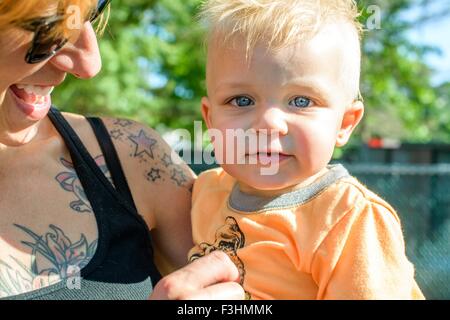 Kopf und Schultern der tätowierte Mutter Baby junge Blick in die Kamera halten Stockfoto