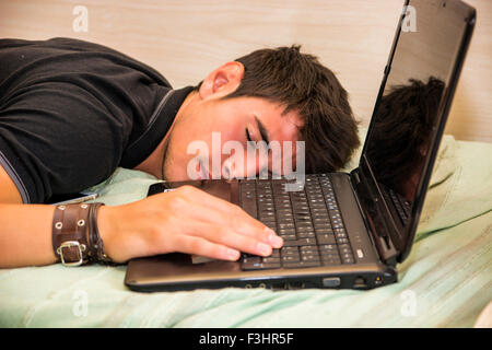 Nahaufnahme von müde junger Mann mit dunklen Haaren schlafen am Boden neben Laptop-Computer mit der Hand auf der Tastatur Stockfoto