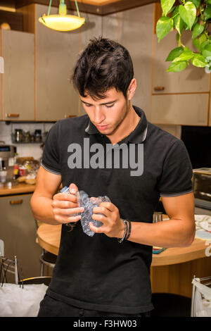 Taille bis attraktive verantwortlich junger Mann mit dunklen Haaren stehen in Küche und vernichtende leer Kunststoff Wasserflasche für Recy Stockfoto