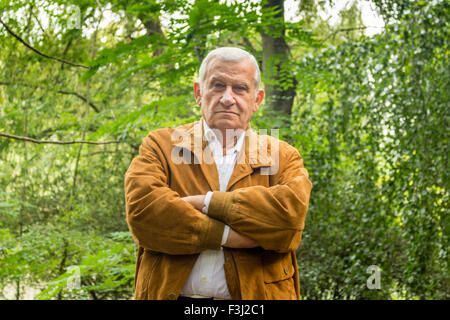 Senior mit Wildleder Jacke und weißes Hemd in einem grünen Park überqueren Arme Stockfoto