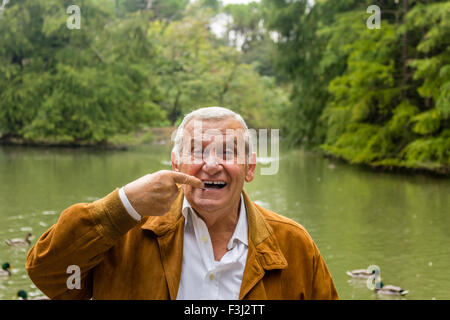 Senior mit Wildleder Jacke und weißes Hemd in einem grünen Park zeigt Zahnersatz Stockfoto