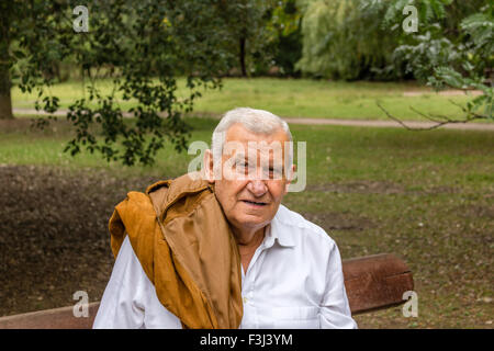 Senior mit Wildlederjacke über Schulter und weißen Hemd in einem grünen park Stockfoto