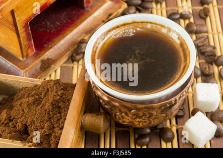 Tasse Kaffee mit Zucker und Kaffee Bohnen, neben gemahlenen Kaffee in einer Mühle-Schublade Stockfoto