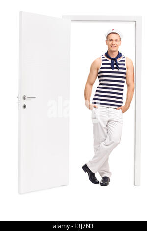 Voller Länge Porträt eines jungen männlichen Matrosen lehnte sich gegen den Rahmen einer offenen Tür isoliert auf weißem Hintergrund Stockfoto