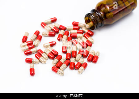 Viele rot und transparent Medizinische capsulas, mit gelben Medizin gefüllt, die aus einer braunen Flasche, auf einem weißen Tabl angezeigt Stockfoto