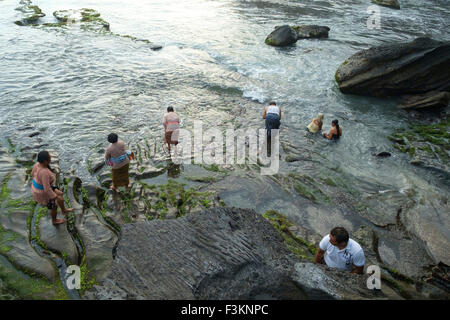 Balinesische Hindu Gläubigen beten bei Sonnenuntergang auf den felsigen Stränden rund um den Tanah Lot Tempel. Stockfoto