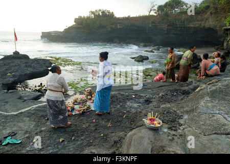 Balinesische Hindu Gläubigen beten bei Sonnenuntergang auf den felsigen Stränden rund um den Tanah Lot Tempel. Stockfoto