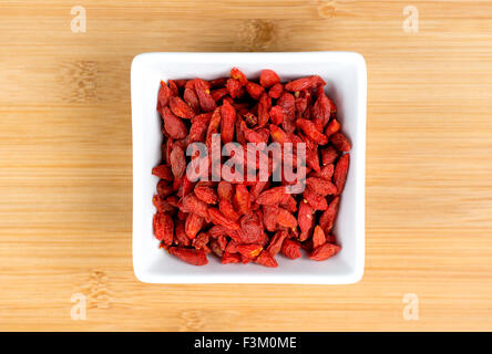 Makroaufnahme einer dehydrierten roten Goji-Beeren in weißen Bowl gegen Holzbrett Stockfoto