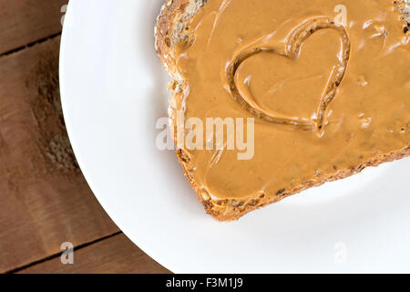 Peanut Butter Toast mit Herzform auf weiß gegen Holzbrett Stockfoto