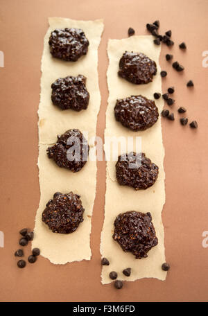 Hausgemachte dunkle Schokolade Kekse künstlerisch auf Pergamentpapier, umgeben von Schokolade-Chips angeordnet. Geringe Schärfentiefe Stockfoto