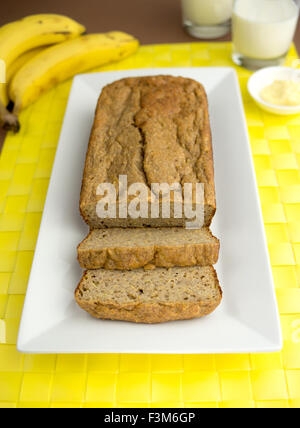 Bananen-Brot-Kuchen mit Scheiben auf einer Platte Rechteck dargestellt. Serviert mit Milch und Butter im Hintergrund gezeigt. Geringe Bautiefe Stockfoto