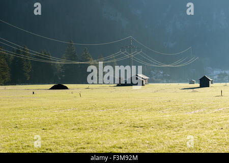 Eine Leitung, überquert einen grean Wiese mit einigen Holzhütten im Morgenlicht Stockfoto