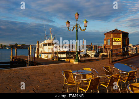 Warmer Sonnenaufgang Sonnenlicht am venezianischen Hafen mit Wasser Taxi Büro freien Tischen und Stühlen und festgemachten Boote Venedig Italien Stockfoto