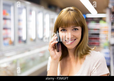 Fröhliche junge Frau auf Smart-Phone im Supermarkt. aussehende Kamera Stockfoto